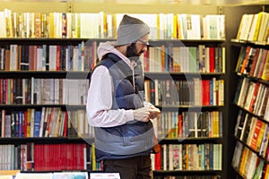 A young man with glasses and a hat in a bookstore selects literature. Education and study
