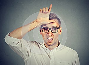 Young man in glasses showing loser sign on forehead