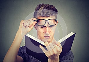Young man with glasses suffering from eyestrain reading a book having vision problems