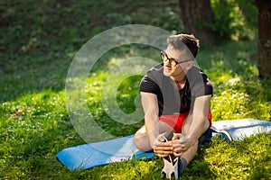Young man in glasses training yoga outdoors. Sporty guy makes relaxing exercise on a blue yoga mat, in park. Copy space