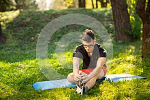 Young man in glasses training yoga outdoors. Sporty guy makes relaxing exercise on a blue yoga mat, in park. Copy space