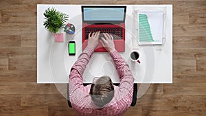 Young man in glasses typing on laptop and using phone with chroma key, topshot, sitting behind desk