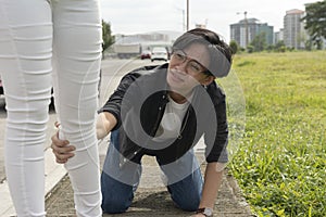 A young man goes down on his knees and grabs the leg of his girlfriend, looking apologetic after making a huge mistake. A