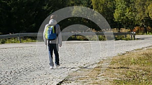 Young man going down empty road in mountains looking around, active tourism