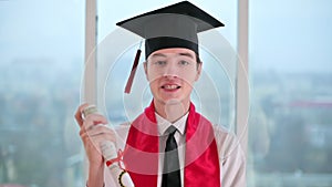 Young man with graduation diploma talking towards the camera. Graduating online in virtual ceremony