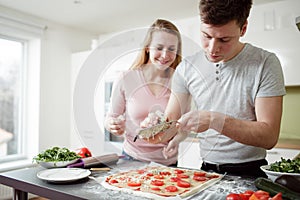 Young man is grating cheese on the pizza.