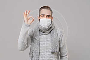 Young man in gray sweater, scarf isolated on grey background. Healthy lifestyle, ill sick disease treatment, cold season