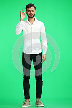 A young man on a green background shows an ok sign in full growth