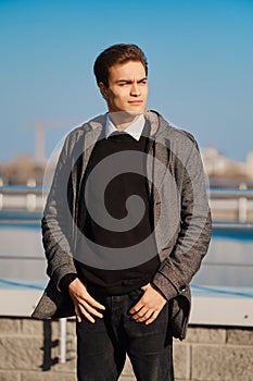 Young man in grey coat, black jumper, white shirt and black jeans