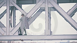 Young man in a grey coat climb on the bridge span