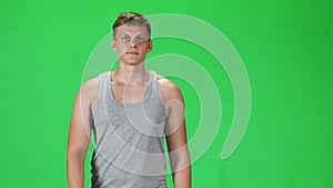 Young man in a grey singlet going and looking forward against a green background. Slow motion.