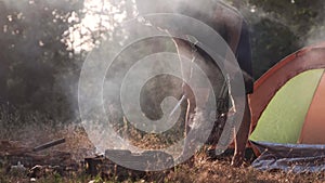 A young man is grilling meat on a fire in the forest.