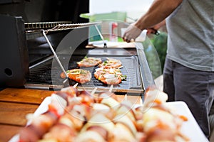 Young man grills some kind of marinated meat and vegetable on gas grill during summer time, food concept