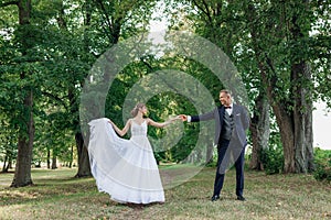 Young man groom holding hand of young pretty woman looking at each other, bride lifting edge of dress. Wedding, dancing.