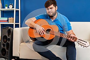 Young man guitar player sitting and performing on a couch