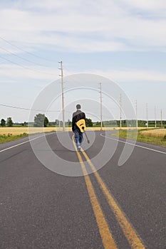 Young man with guitar walking down middle of Road