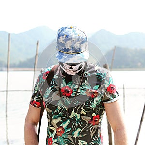 Young man guy in casual t-shirt, cap and face mask posing on nature background. Traveling lifestyle concept. Bearded Young Man