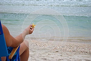 Young man guy sitting on a deckchair on the shore holding a yellow starfish in his hand