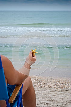 Young man guy sitting on a deckchair on the shore holding a yellow starfish in his hand