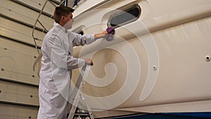 A young man guy is a specialist in cleaning the yacht, in a respirator and using a spray on the background of the yachts. Concep