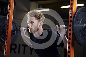 Young Man In Gym Lifting Weights On Barbell