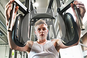 Young man in gym working out, using weights machine.