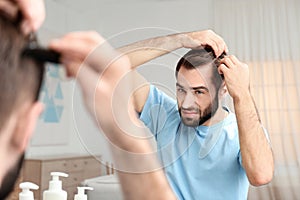 Young man with hair loss problem in front of mirror