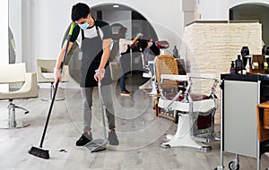 Young man hairdresser in mask cleaning floor