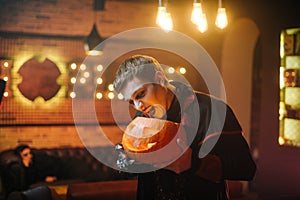 Young man in a Halloween costume of Count Dracula holds a carved festive pumpkin