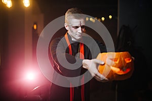 Young man in a Halloween costume holding a carved pumpkin on his outstretched arm