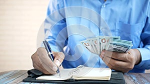 young man hand holding cash and writing on notepad