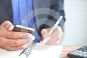 young man hand using smart phone and writing on a notepad on office desk