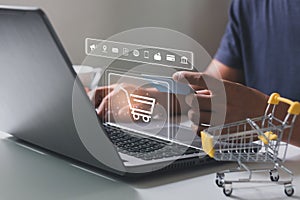 Young man hands holding credit card and using laptop with shopping cart icon.