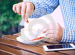 Young man hands holding sugar bag and sweetens coffee in a cafe.