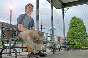 Young man happily sits on park bench with a beaming light pole lighting up the evening sky behind him.