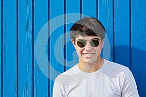 Young man happy man in sunglasses against blue wooden wall