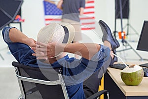 Young man happy wearing a hat and sitting on a chair, placing both hands on the back of the neck for relaxing and foot on the desk