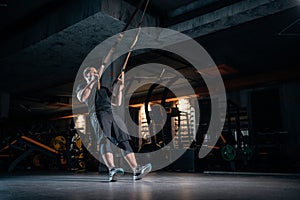 Young man has crossfit workout with trx in modern gym