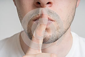 Young man has finger on lips and showing be quiet gesture photo