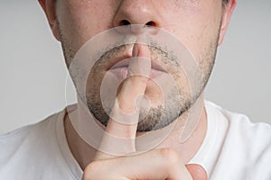 Young man has finger on lips and showing be quiet gesture photo