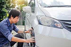 Young man has problems with the wheel of his car. He is kneeing and Check tires before leaving.man checking car condition photo