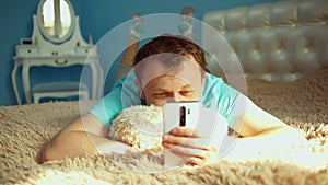 The young man has a rest lies on a bed in a bedroom with a mobile phone in hands