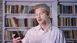 Young man has video call on smartphone in library, communication concept