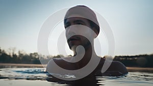 Young man in hat bathing in the ice water alone at the morning