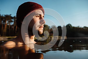 Young man in hat bathing in the ice water alone at the morning