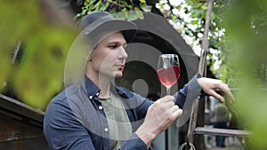 young man in a hat drinking red wine in a vineyard.