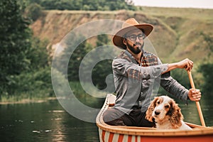 Young man in hat on the river in wooden canoe with his dog