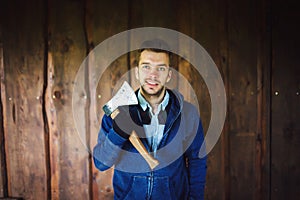 Young man with a hatchet in front of wooden wall
