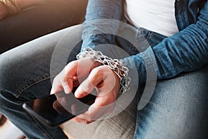 Young man have social media addiction. Phone in hands. Chains around wrist. Hostage of social media. Sitting on sofa