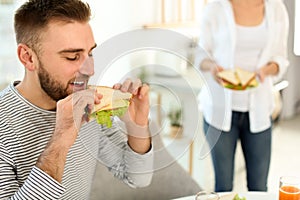 Young man having breakfast with sandwiches in kitchen